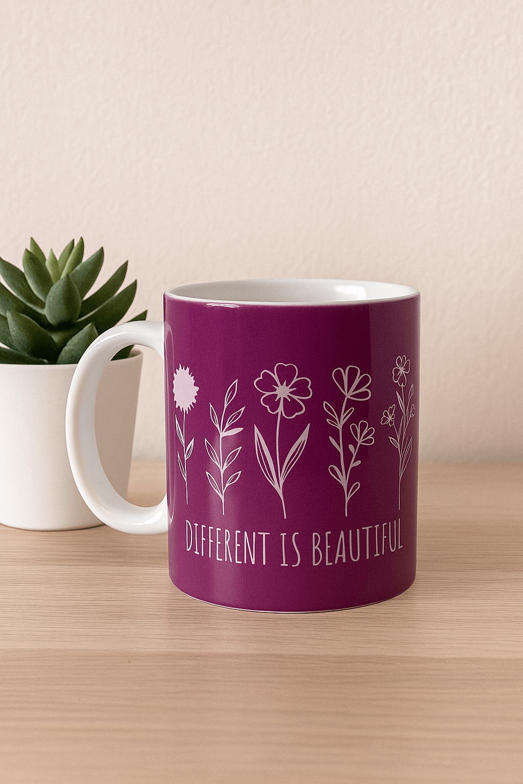 Purple mug with floral design and 'Different is Beautiful' text on a wooden surface with a plant in the background.